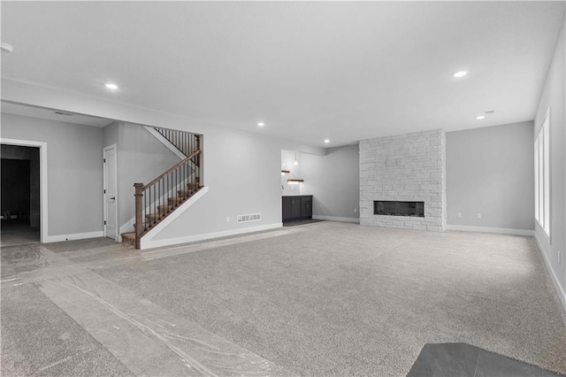 unfurnished living room featuring recessed lighting, light colored carpet, a fireplace, and stairway