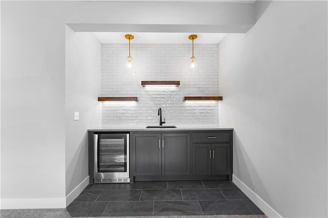 bar with wine cooler, a sink, baseboards, hanging light fixtures, and backsplash