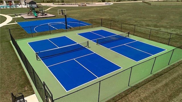 view of tennis court featuring fence, a lawn, and playground community