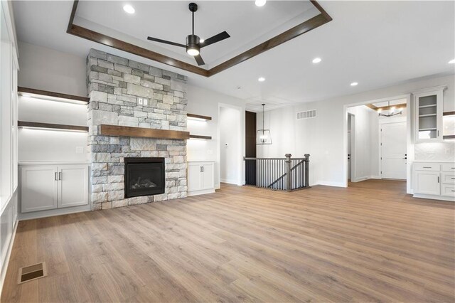 1617 SW Arbor Park Dr, Lees Summit, MO 64082 - unfurnished living room featuring a tray ceiling, light wood-style flooring, a ceiling fan, recessed lighting, and a fireplace