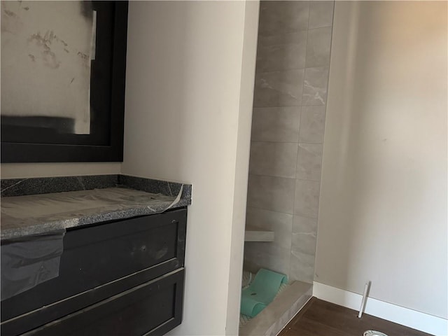 bathroom with a shower, wood finished floors, vanity, and baseboards