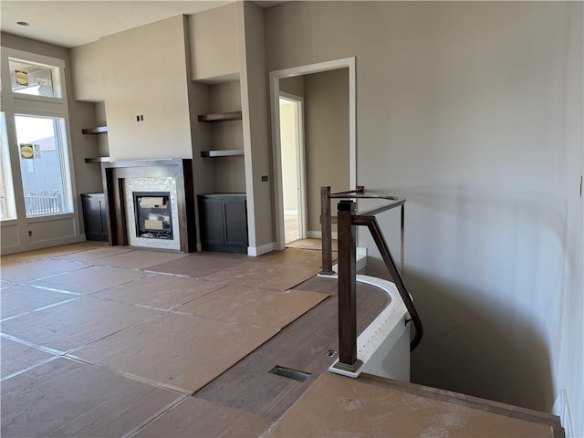 living area featuring baseboards, built in features, and a glass covered fireplace