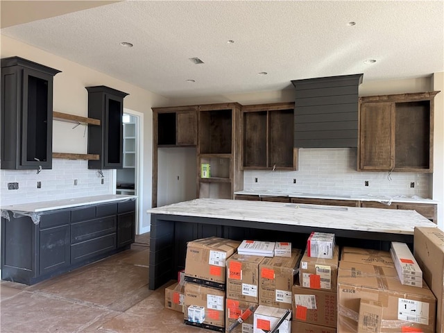 kitchen featuring a textured ceiling, light stone counters, a kitchen island, open shelves, and tasteful backsplash