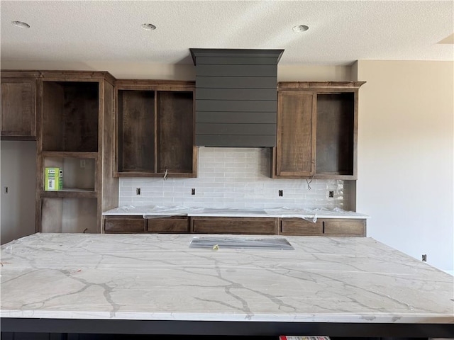 kitchen featuring tasteful backsplash, a textured ceiling, light stone counters, and dark brown cabinets