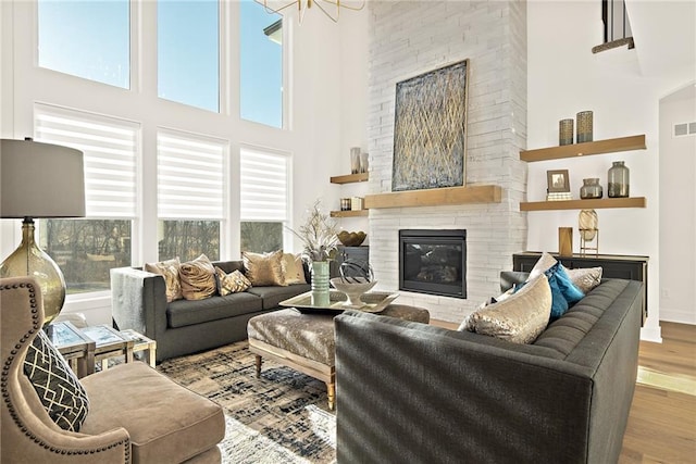 living room featuring a high ceiling, wood-type flooring, and a stone fireplace