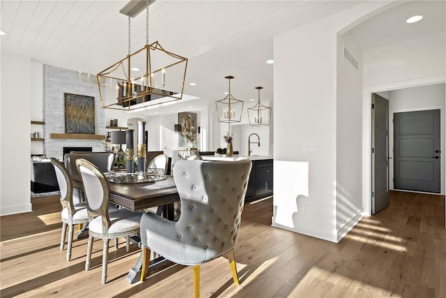 dining area with sink, wood-type flooring, wooden ceiling, an inviting chandelier, and a fireplace