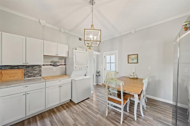 kitchen featuring hanging light fixtures, white cabinetry, stacked washer and clothes dryer, light wood-type flooring, and a chandelier