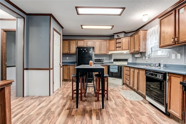 kitchen featuring ornamental molding, black appliances, under cabinet range hood, a sink, and light wood finished floors