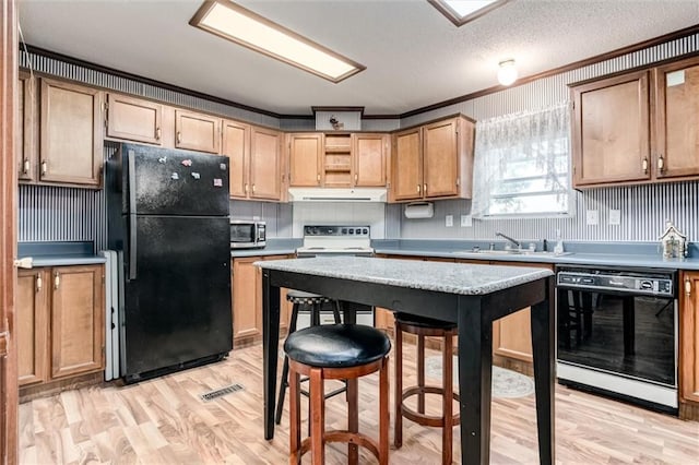 kitchen featuring light wood-style flooring, ornamental molding, black appliances, under cabinet range hood, and a sink