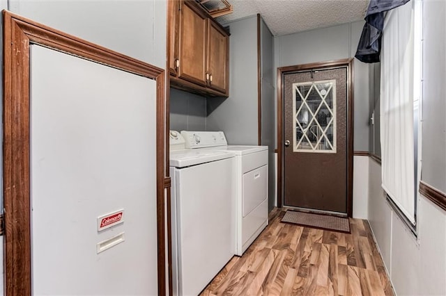 laundry room with a textured ceiling, light wood-type flooring, washing machine and clothes dryer, and cabinet space