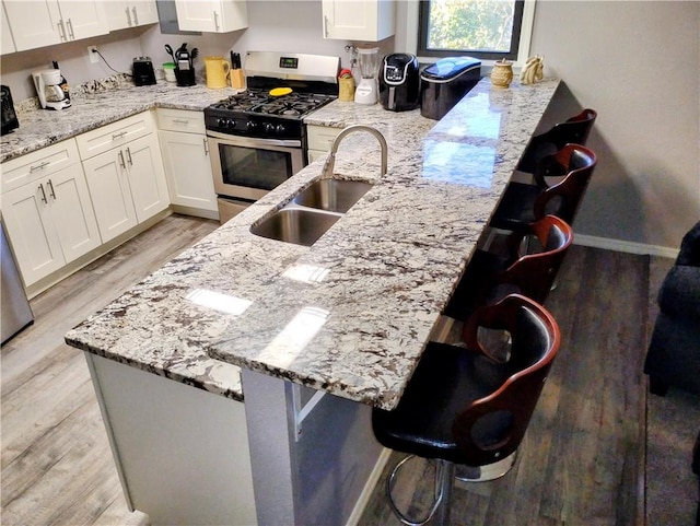 kitchen with stainless steel gas range oven, sink, white cabinetry, a breakfast bar area, and light stone counters