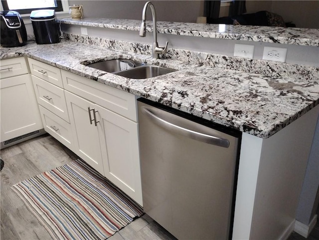 kitchen with dishwasher, white cabinetry, sink, light stone counters, and light hardwood / wood-style flooring