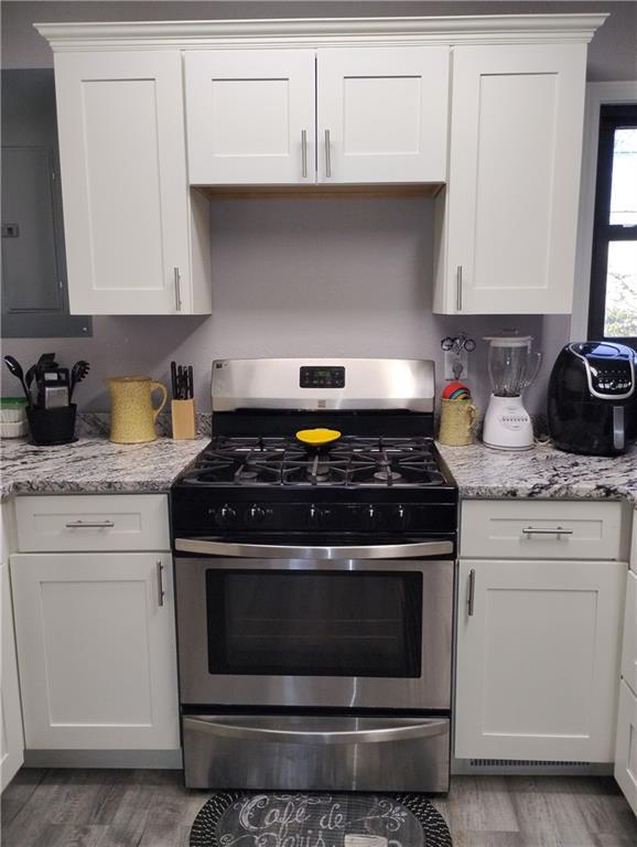 kitchen with stainless steel gas stove, light stone counters, white cabinetry, and light hardwood / wood-style flooring