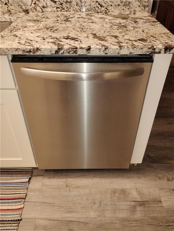 interior details featuring stainless steel dishwasher, white cabinets, and light stone counters