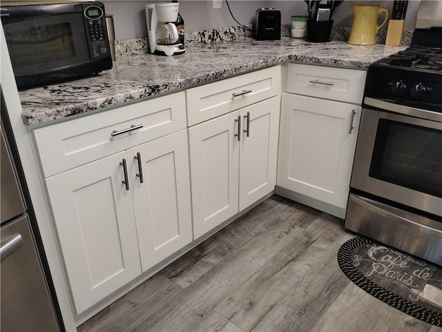 kitchen with light stone countertops, appliances with stainless steel finishes, white cabinetry, and light hardwood / wood-style flooring