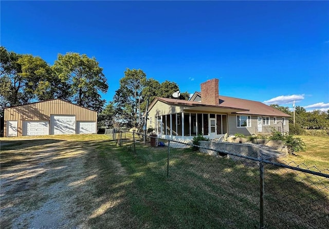 rear view of property with a detached garage, fence, a lawn, a chimney, and an outbuilding