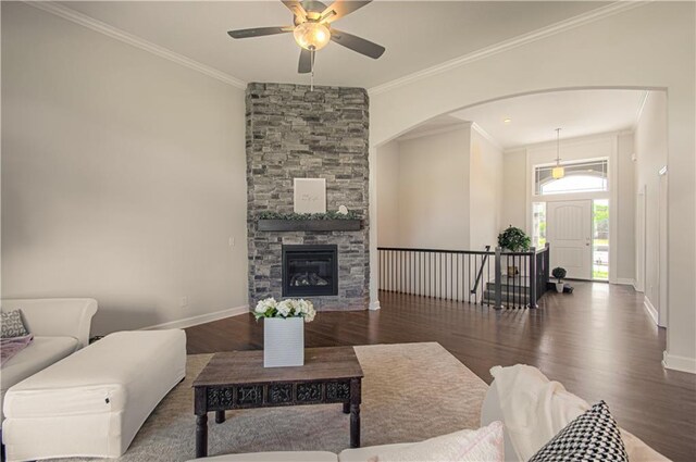 living room with a stone fireplace, crown molding, ceiling fan, and dark wood-type flooring