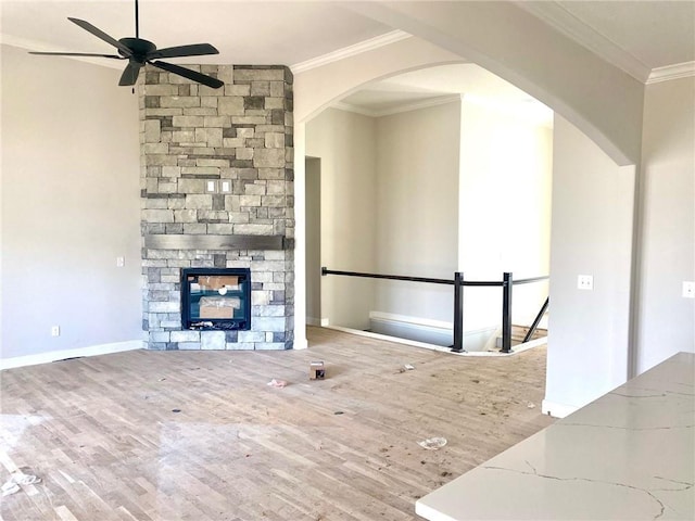 unfurnished living room featuring a stone fireplace, wood finished floors, arched walkways, and ornamental molding