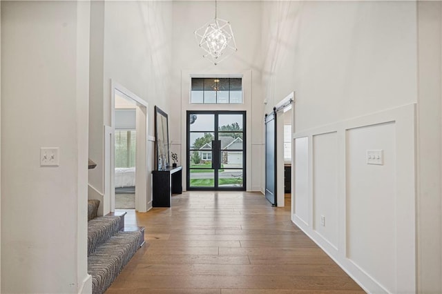 entryway with a chandelier, a barn door, a towering ceiling, hardwood / wood-style floors, and french doors