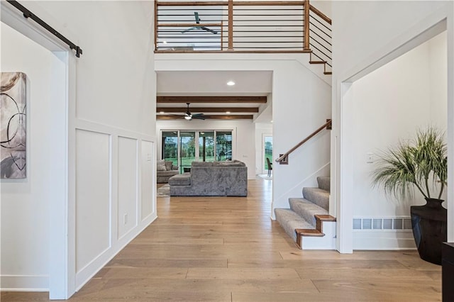 entrance foyer featuring a high ceiling, light hardwood / wood-style floors, beamed ceiling, and a barn door