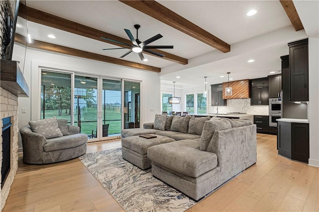 living room featuring light wood-type flooring, beam ceiling, ceiling fan, and a fireplace