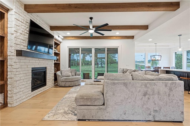 living room featuring light hardwood / wood-style flooring, beam ceiling, ceiling fan, and a fireplace