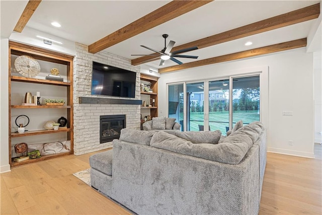 living room with light hardwood / wood-style flooring, ceiling fan, beamed ceiling, and a fireplace