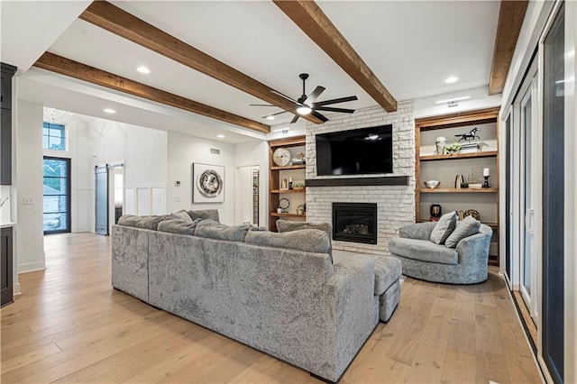 living room featuring a fireplace, beam ceiling, ceiling fan, and light hardwood / wood-style flooring