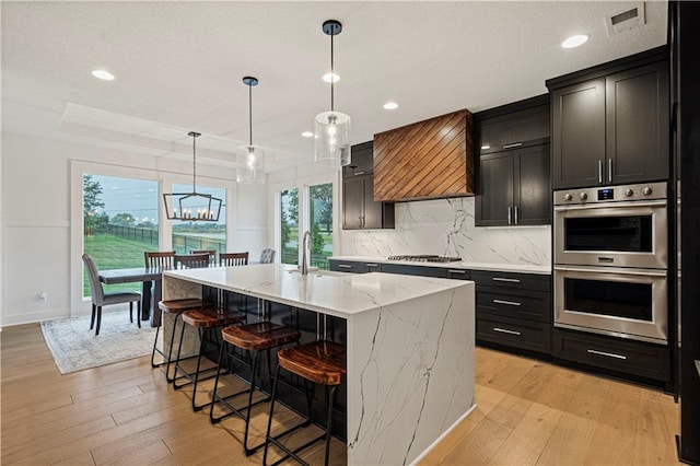 kitchen with an island with sink, pendant lighting, appliances with stainless steel finishes, and light hardwood / wood-style flooring