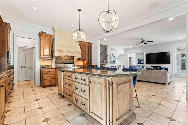 kitchen featuring a kitchen island, custom range hood, ceiling fan with notable chandelier, hanging light fixtures, and a breakfast bar area