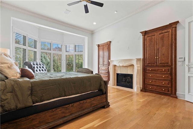 bedroom with light wood-type flooring, a tiled fireplace, ceiling fan, and crown molding