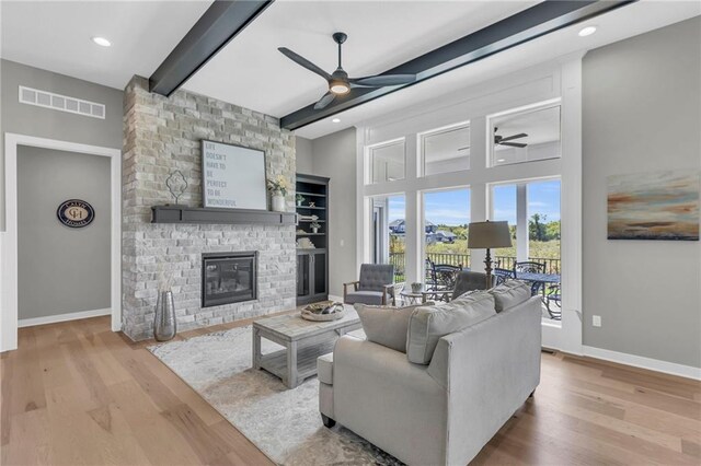 living room with light hardwood / wood-style flooring, beam ceiling, a fireplace, and ceiling fan