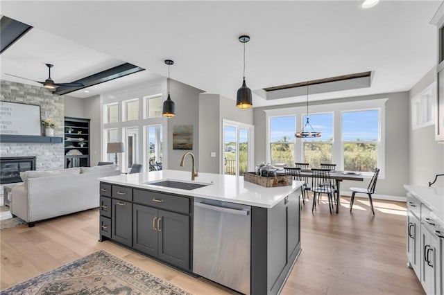 kitchen with light hardwood / wood-style flooring, decorative light fixtures, stainless steel dishwasher, and a center island with sink