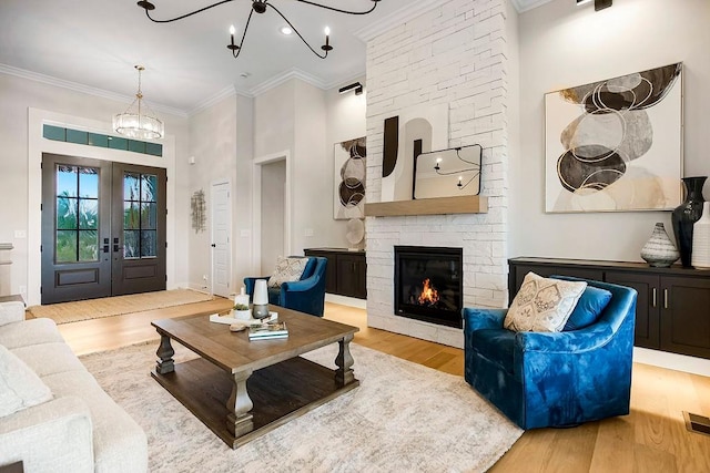 living room with french doors, a stone fireplace, a chandelier, light wood-type flooring, and crown molding