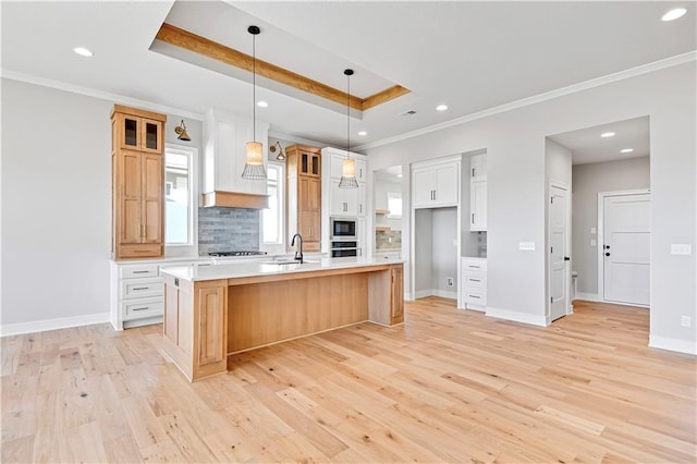 kitchen with a raised ceiling, appliances with stainless steel finishes, light countertops, premium range hood, and backsplash