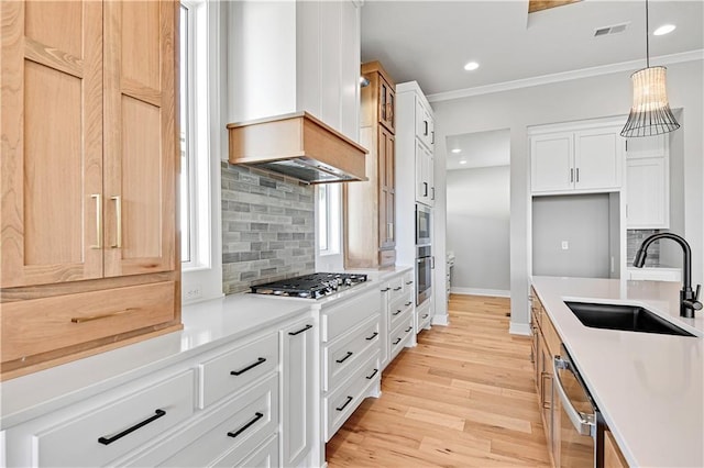 kitchen featuring a sink, stainless steel appliances, crown molding, light wood-type flooring, and backsplash