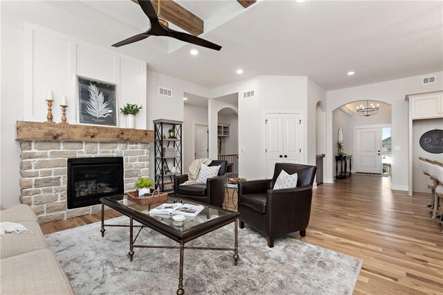 living room with light wood-type flooring, ceiling fan with notable chandelier, and a stone fireplace