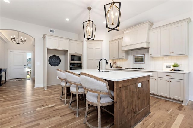 kitchen with pendant lighting, light hardwood / wood-style flooring, a kitchen island with sink, sink, and a chandelier