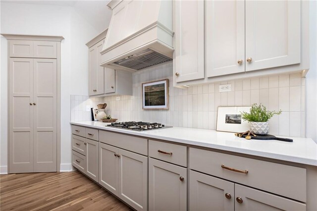 kitchen with premium range hood, gray cabinetry, light hardwood / wood-style flooring, backsplash, and stainless steel gas stovetop