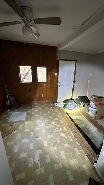 unfurnished living room featuring ceiling fan and wood walls