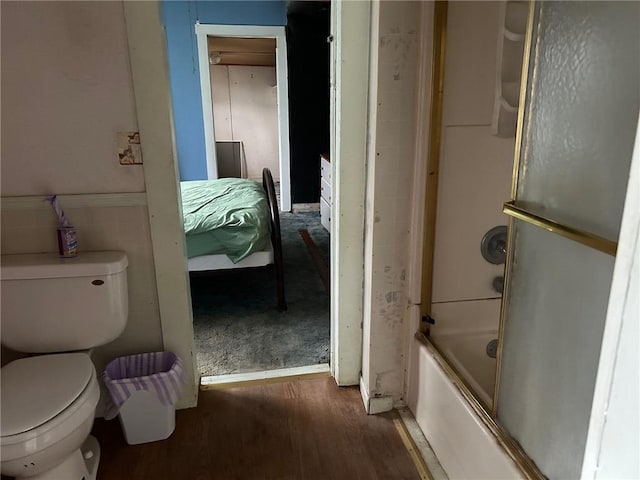 bathroom featuring wood-type flooring, bath / shower combo with glass door, and toilet