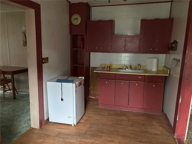 kitchen with light wood-type flooring, backsplash, sink, and white refrigerator