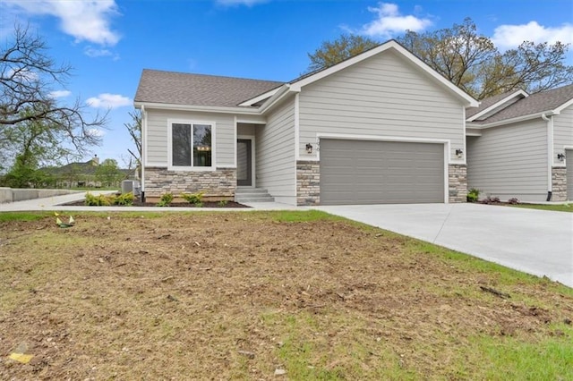 view of front of property featuring a garage, stone siding, a shingled roof, concrete driveway, and central air condition unit