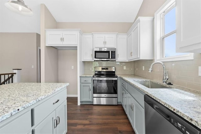 kitchen with dark wood-style flooring, white cabinets, light stone counters, a sink, and appliances with stainless steel finishes
