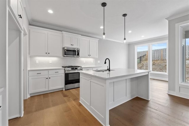 kitchen featuring hanging light fixtures, stainless steel appliances, an island with sink, white cabinets, and sink