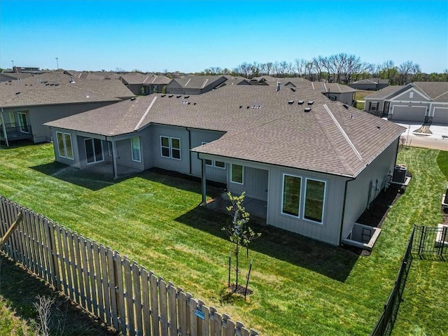 back of house featuring a lawn, roof with shingles, a residential view, and a fenced backyard