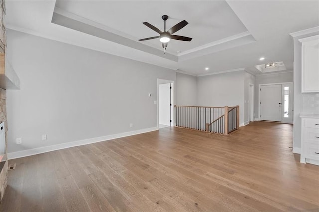 unfurnished living room featuring crown molding, light wood-type flooring, ceiling fan, a tray ceiling, and baseboards