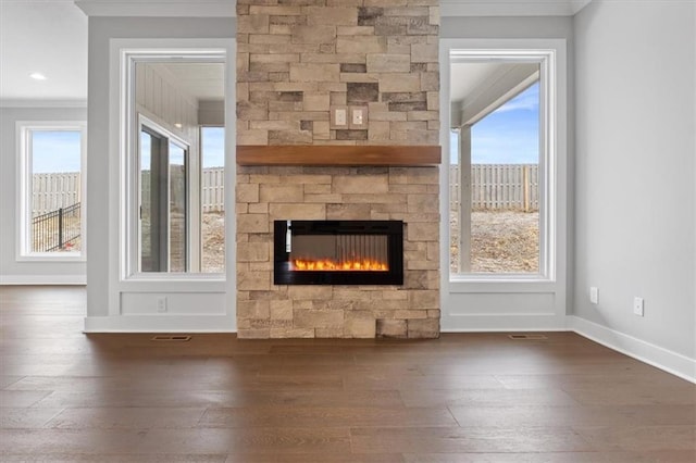 unfurnished living room featuring baseboards, visible vents, crown molding, a stone fireplace, and wood-type flooring