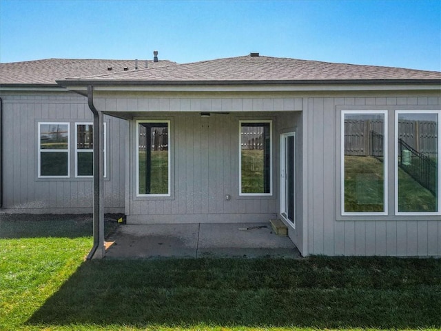 back of house with roof with shingles, a yard, and a patio
