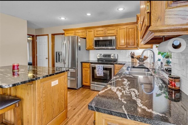 kitchen featuring sink, backsplash, dark stone countertops, appliances with stainless steel finishes, and light wood-type flooring